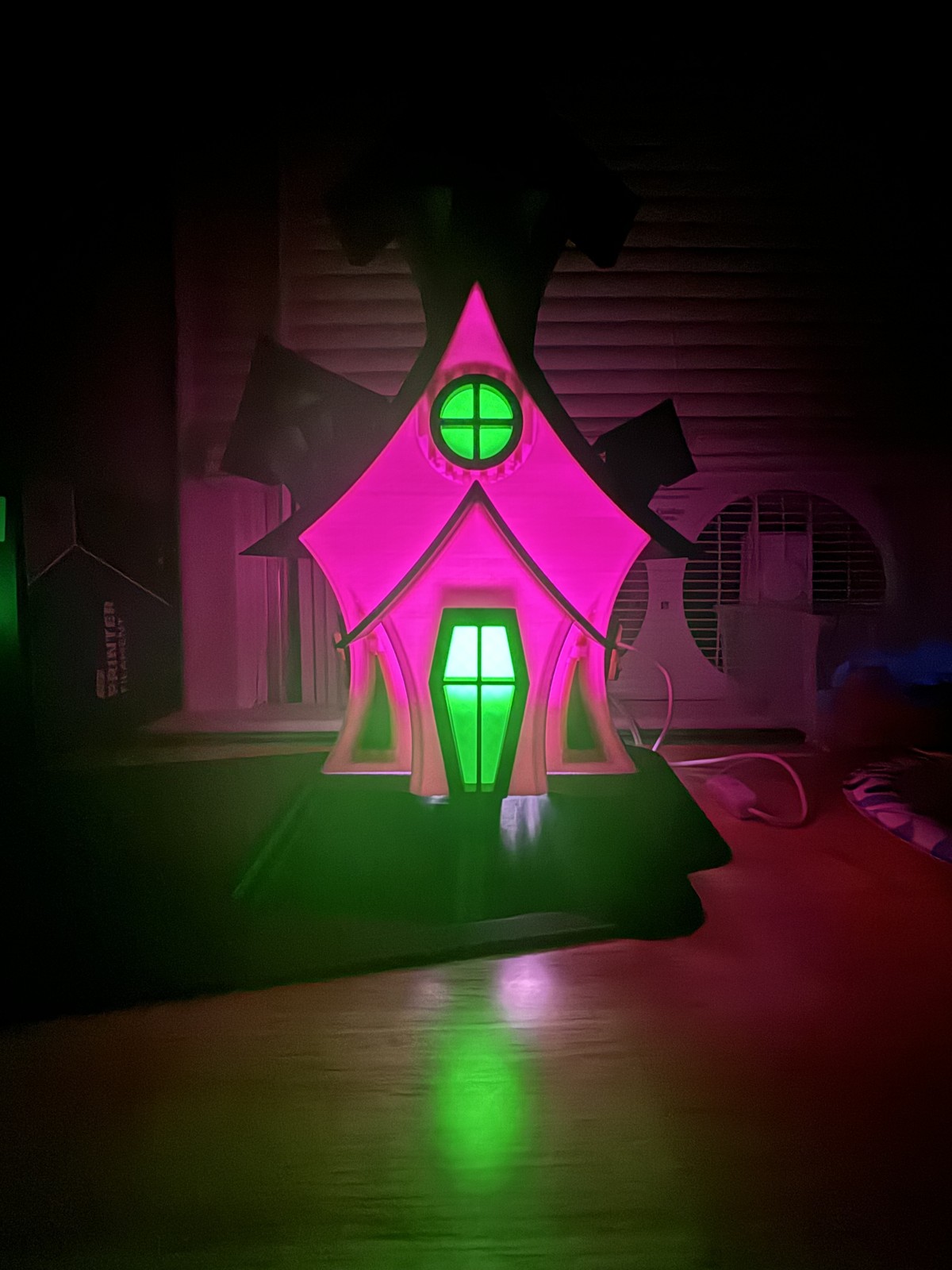 Haunted-house model glowing pink and green in a dark room