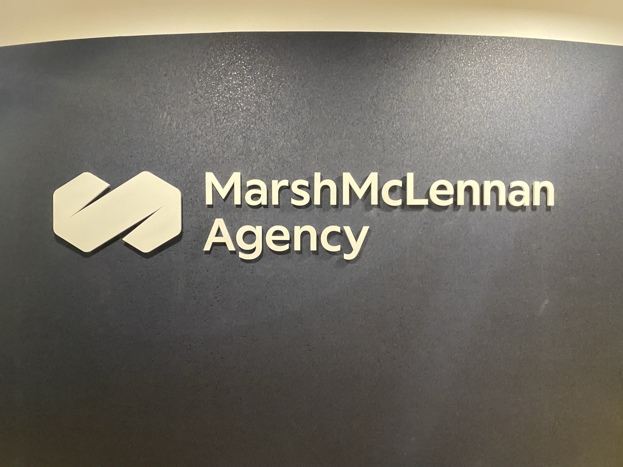 Marsh McLennan Agency dimensional logo and raised lettering on a textured gray wall